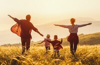 Famille de quatre personnes courant à travers un champ au coucher du soleil, les bras étendus.