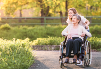 Personne en fauteuil roulant aidée par une autre dans un parc ensoleillé.